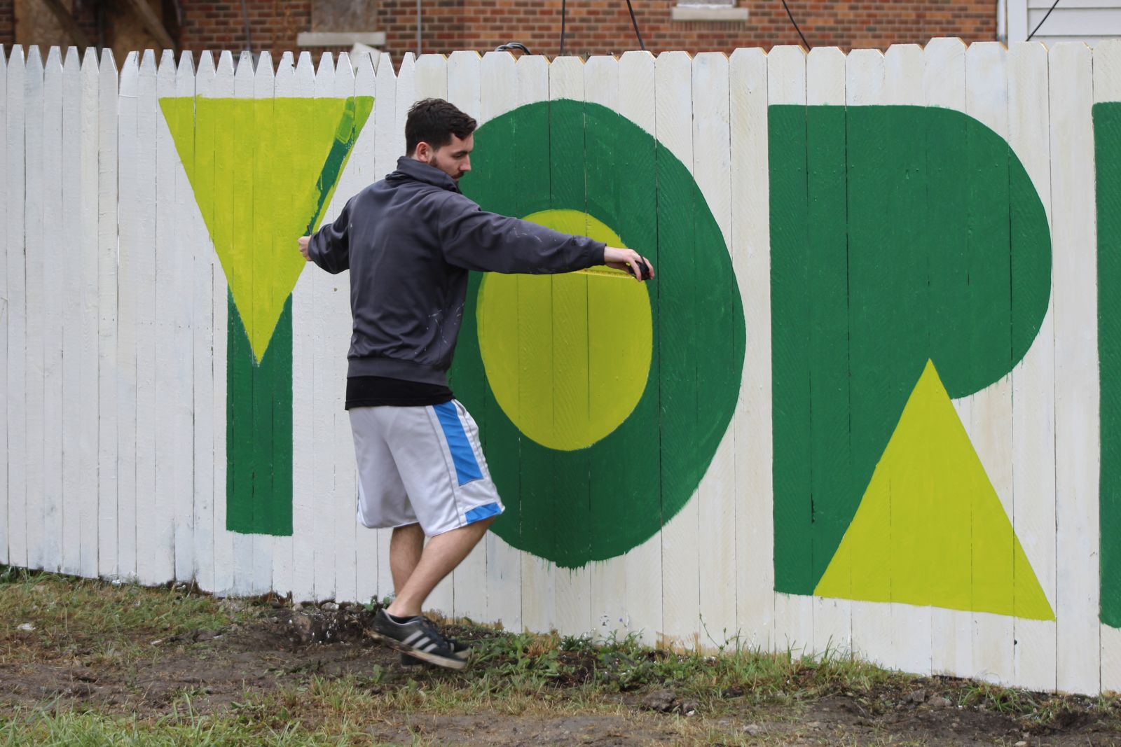A volunteer painting large letters on the Four Angels Garden fence